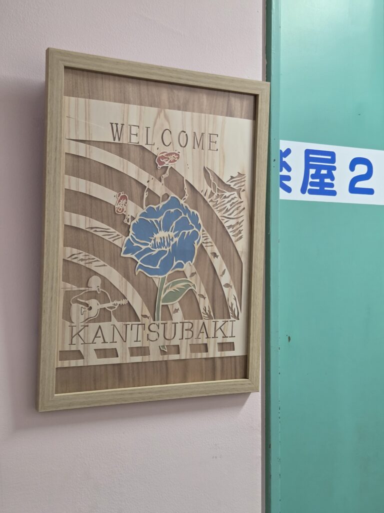 寒椿様への木の切り絵ウェルカムボード。ボーカル吉野様の弾き語りの姿と『クジラの歌』から着想を得た、波とクジラが描かれた切り絵図柄。楽屋表札として使用。