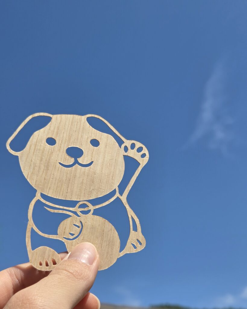 登米市産スギを使用した木製ペットお守り「招きわんこお守り」と青空。